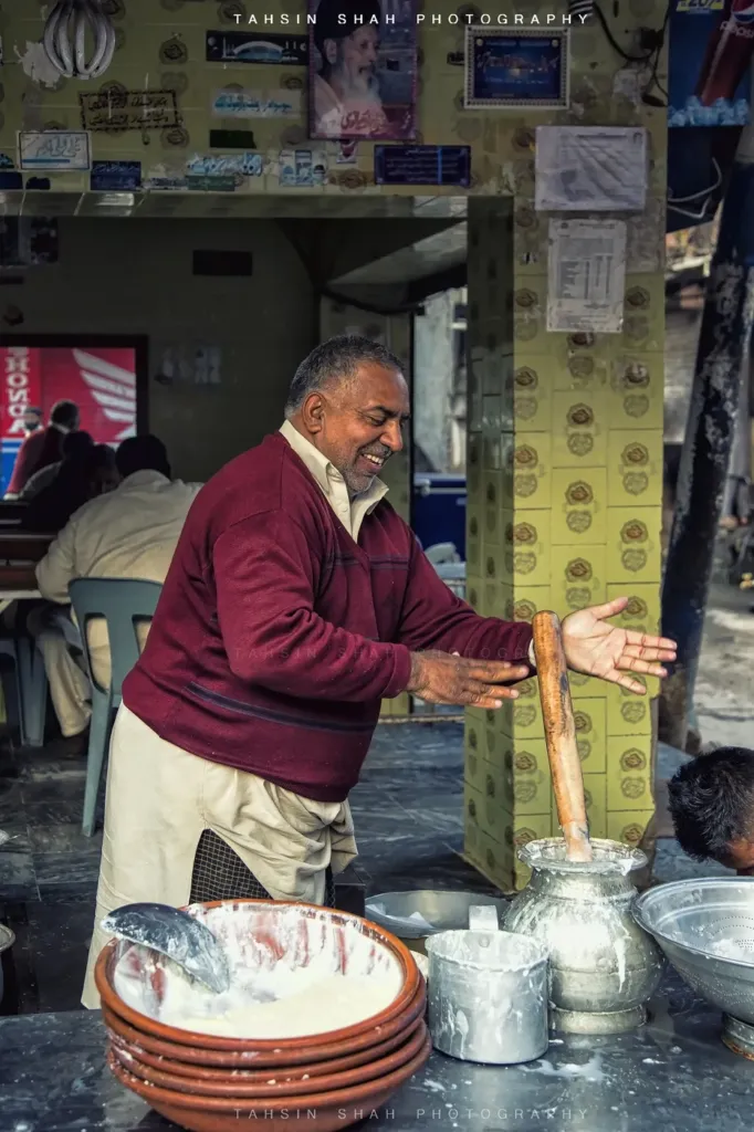 Shopkeeper in Pakistan churning fresh lassi in a steel pot