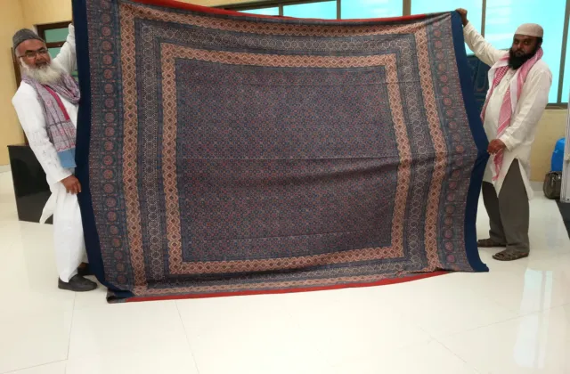 Two men holding up a full-size block-printed Ajrak with indigo field and wide red-and-blue borders
