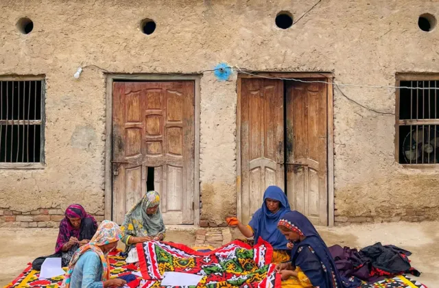 Sindhi women sitting on a colourful rug in Sukkur while working on traditional textiles